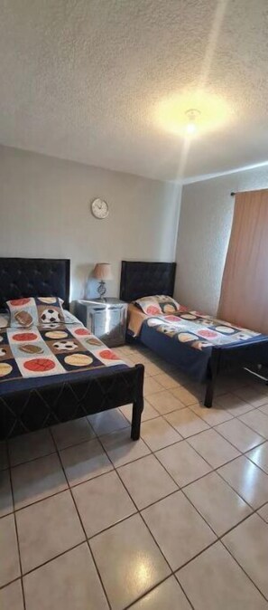Une chambre avec deux lits, une petite table et une horloge au mur.