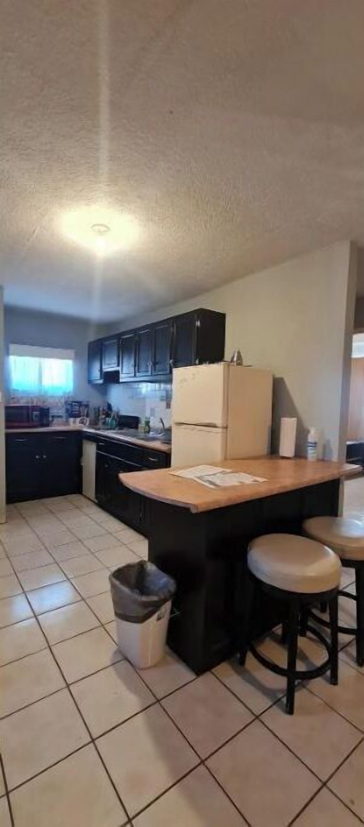 Una cocina con una isla central, armarios oscuros y piso de baldosas.