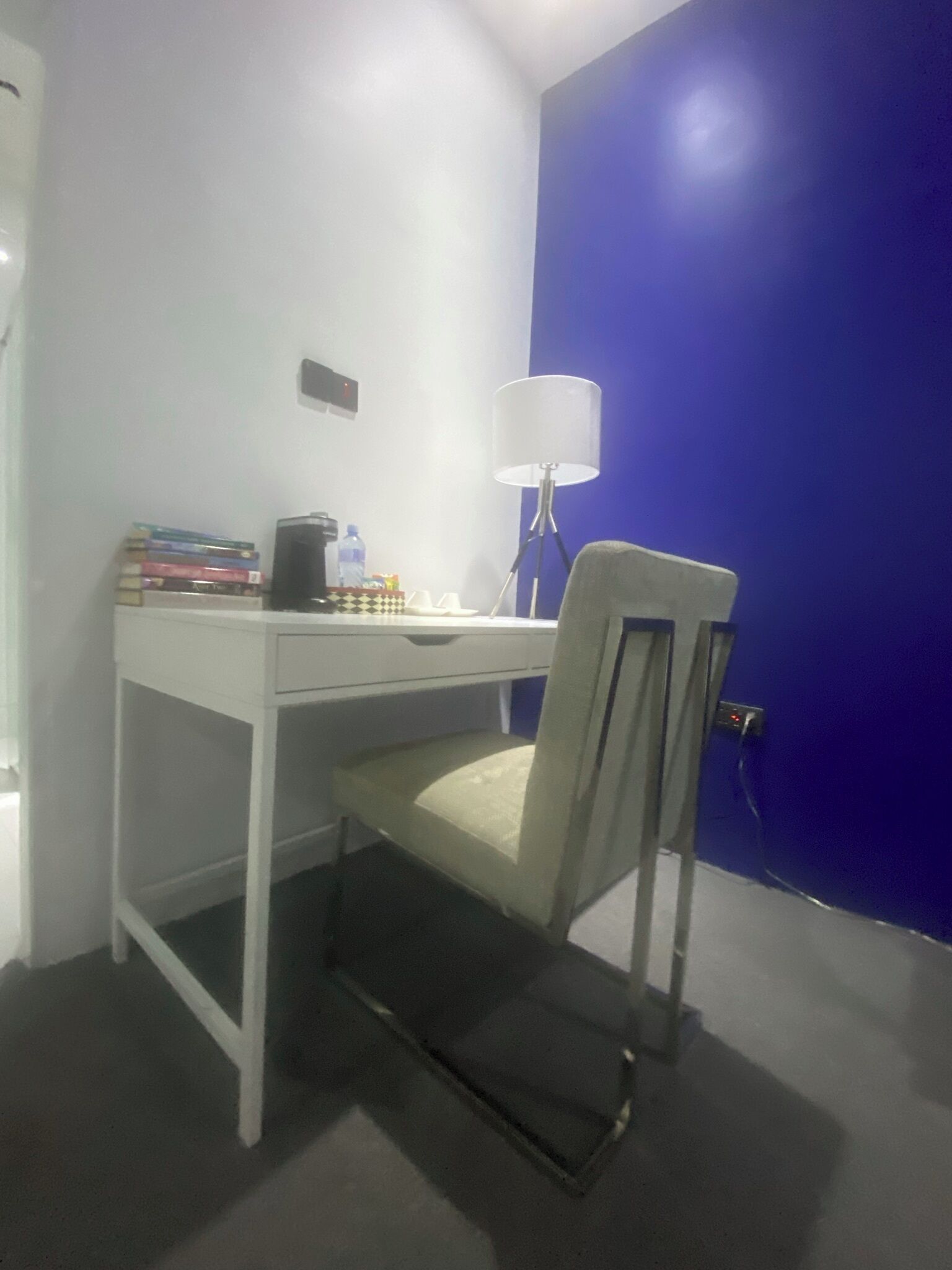 Un pequeño escritorio blanco con una silla, una lámpara y una pila de libros.