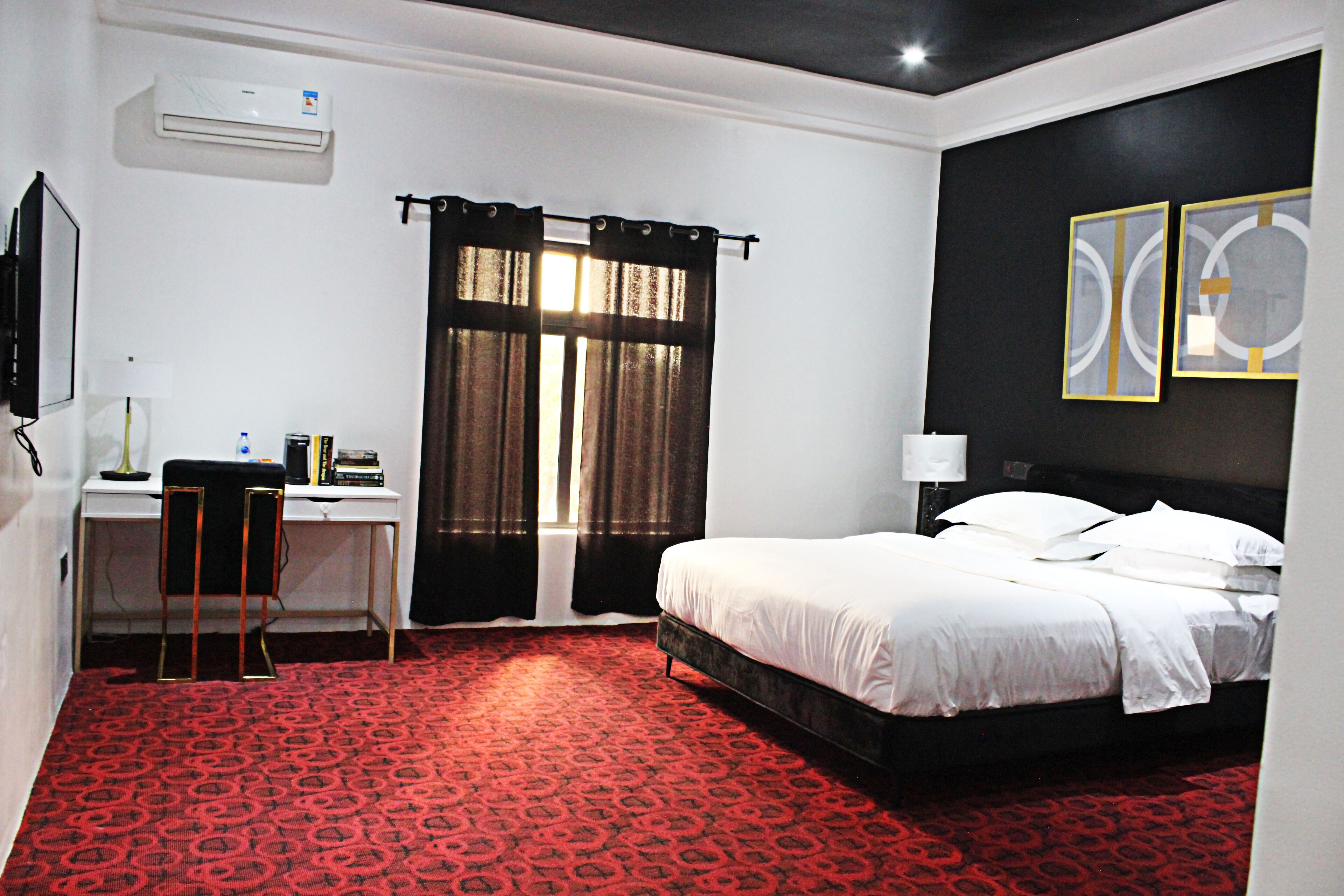 A hotel room with a bed, a desk with a chair, a computer, and a window with curtains.