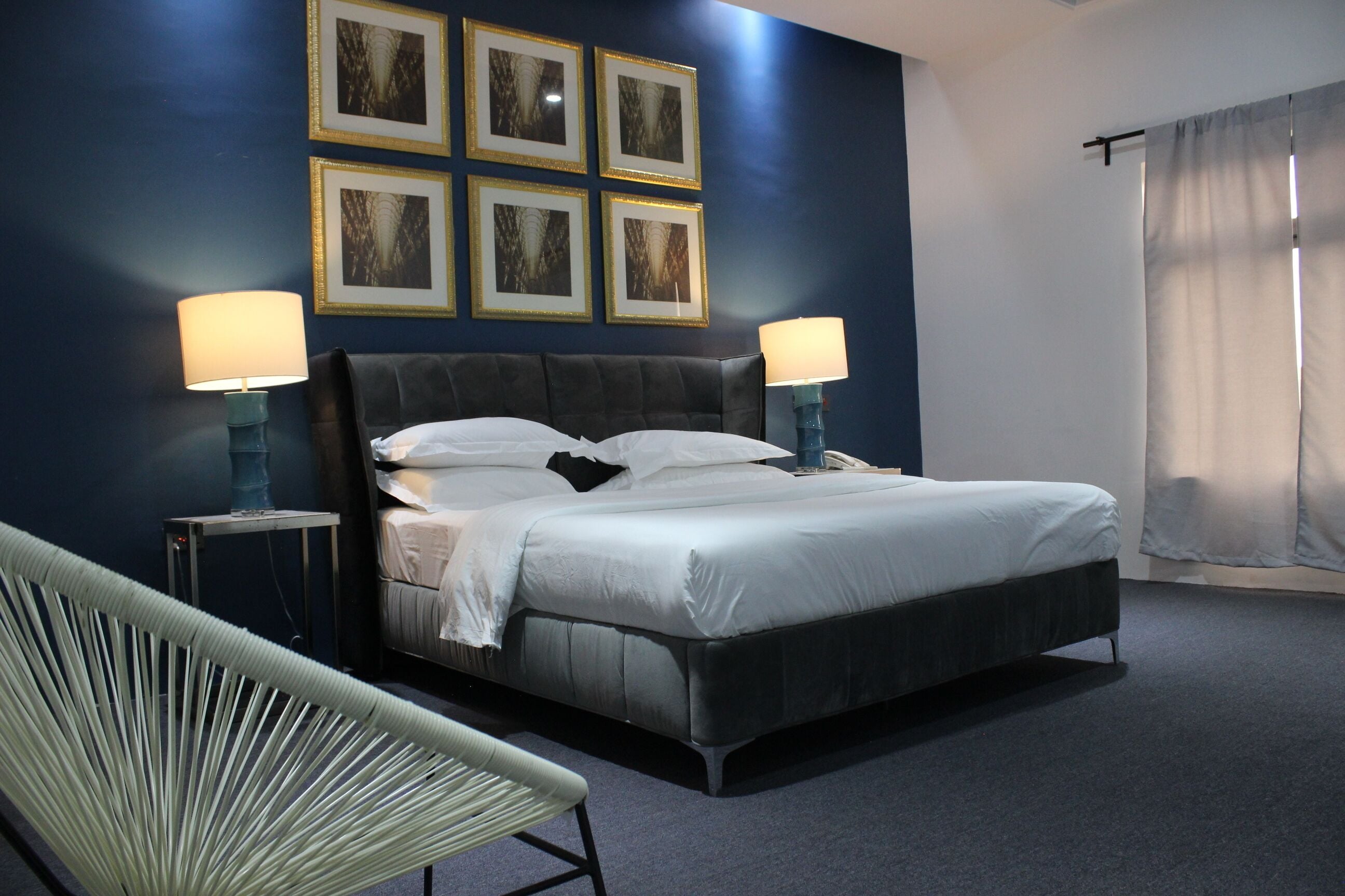 Una habitación de hotel moderna con una cama grande, dos lámparas de noche, una silla y cuadros en la pared.