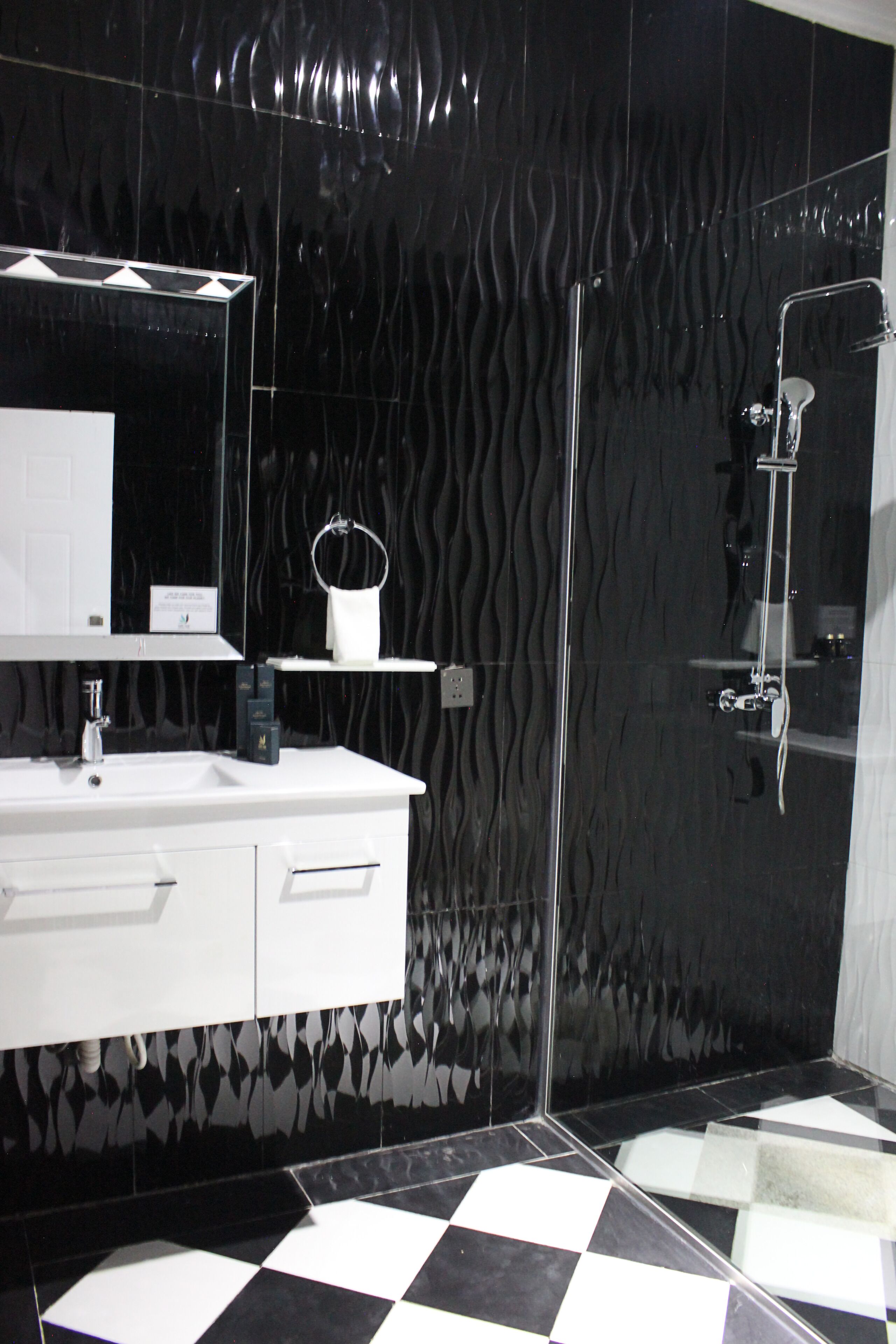 Un baño moderno con piso a cuadros blanco y negro, un tocador blanco con espejo y una pared negra con textura.
