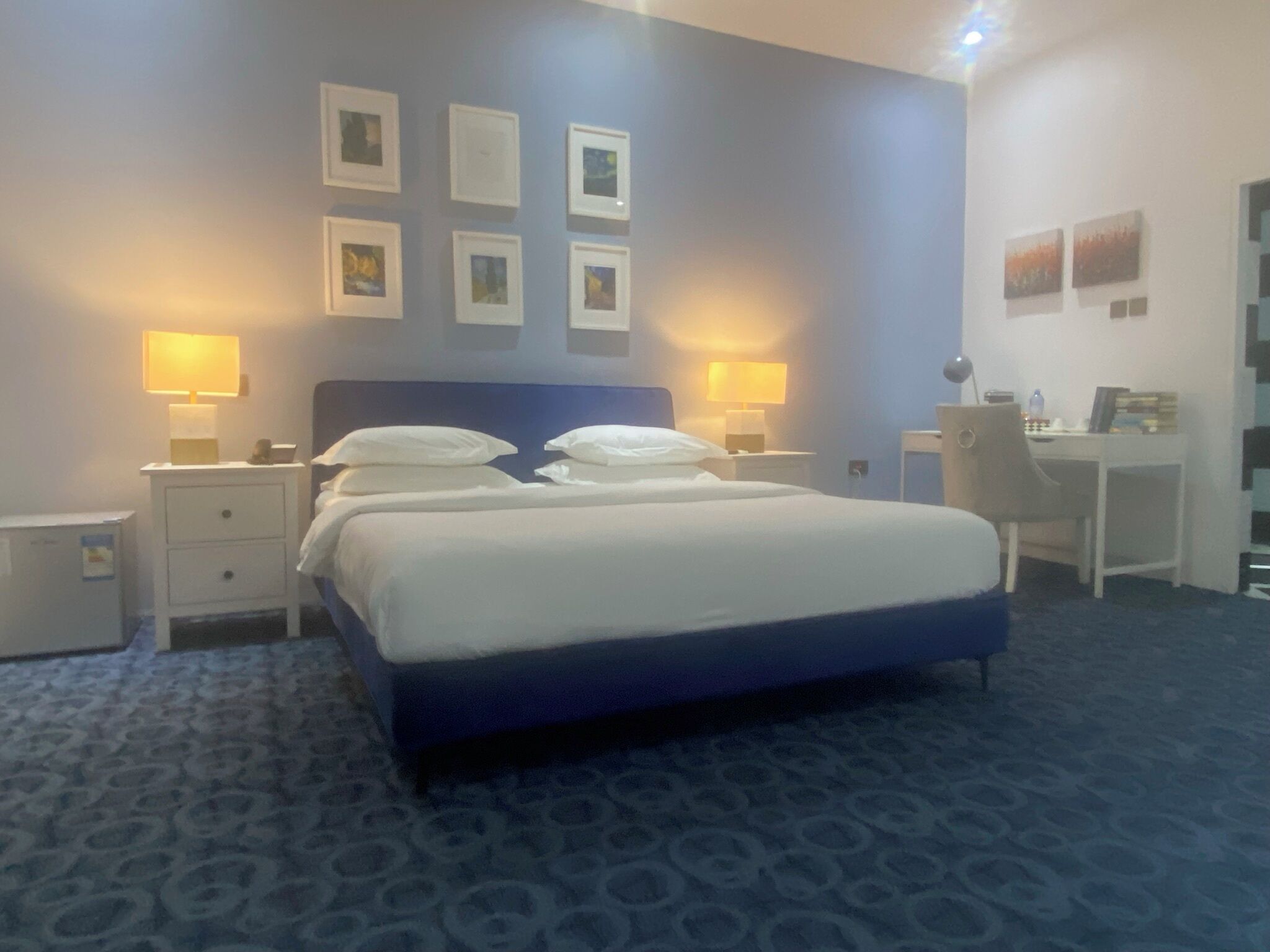 A hotel room with a large bed, two bedside tables with lamps, a desk, and a chair.