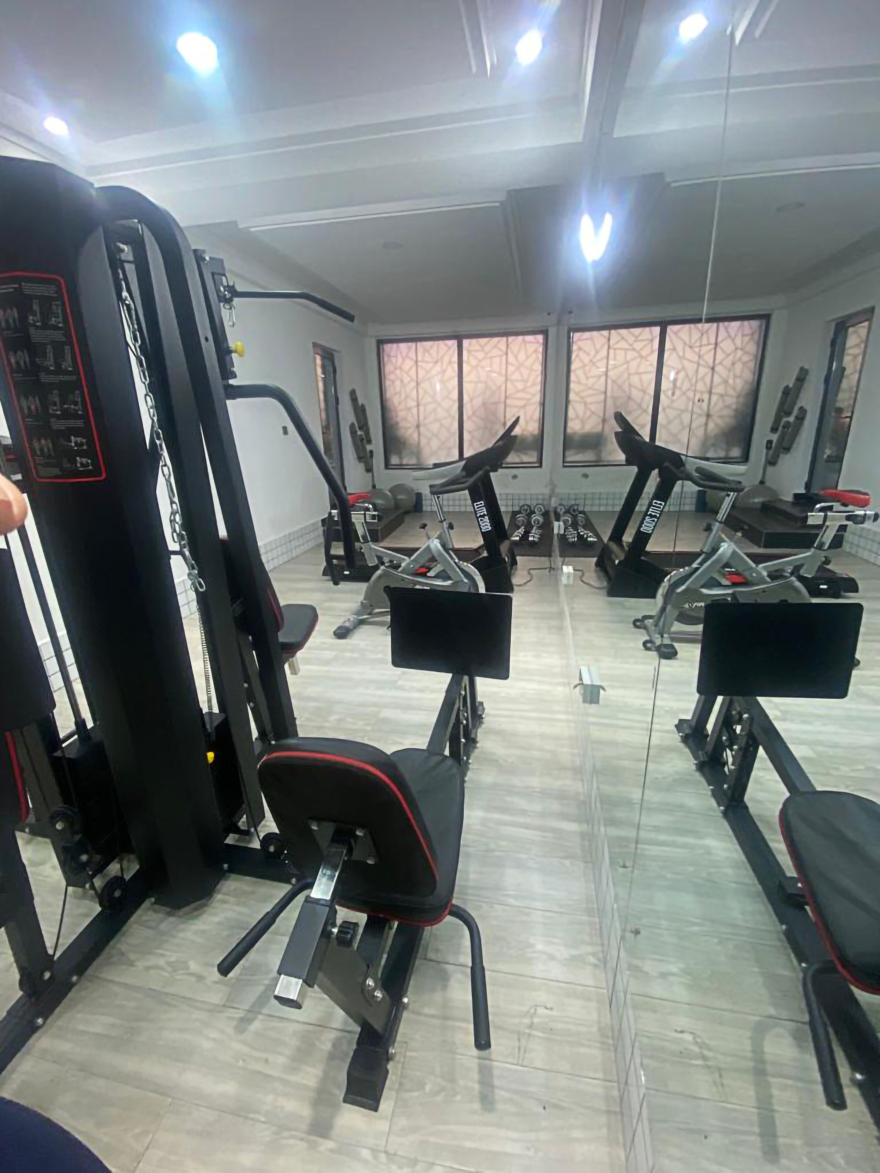 A gym with various exercise machines, large windows, and a tiled floor.
