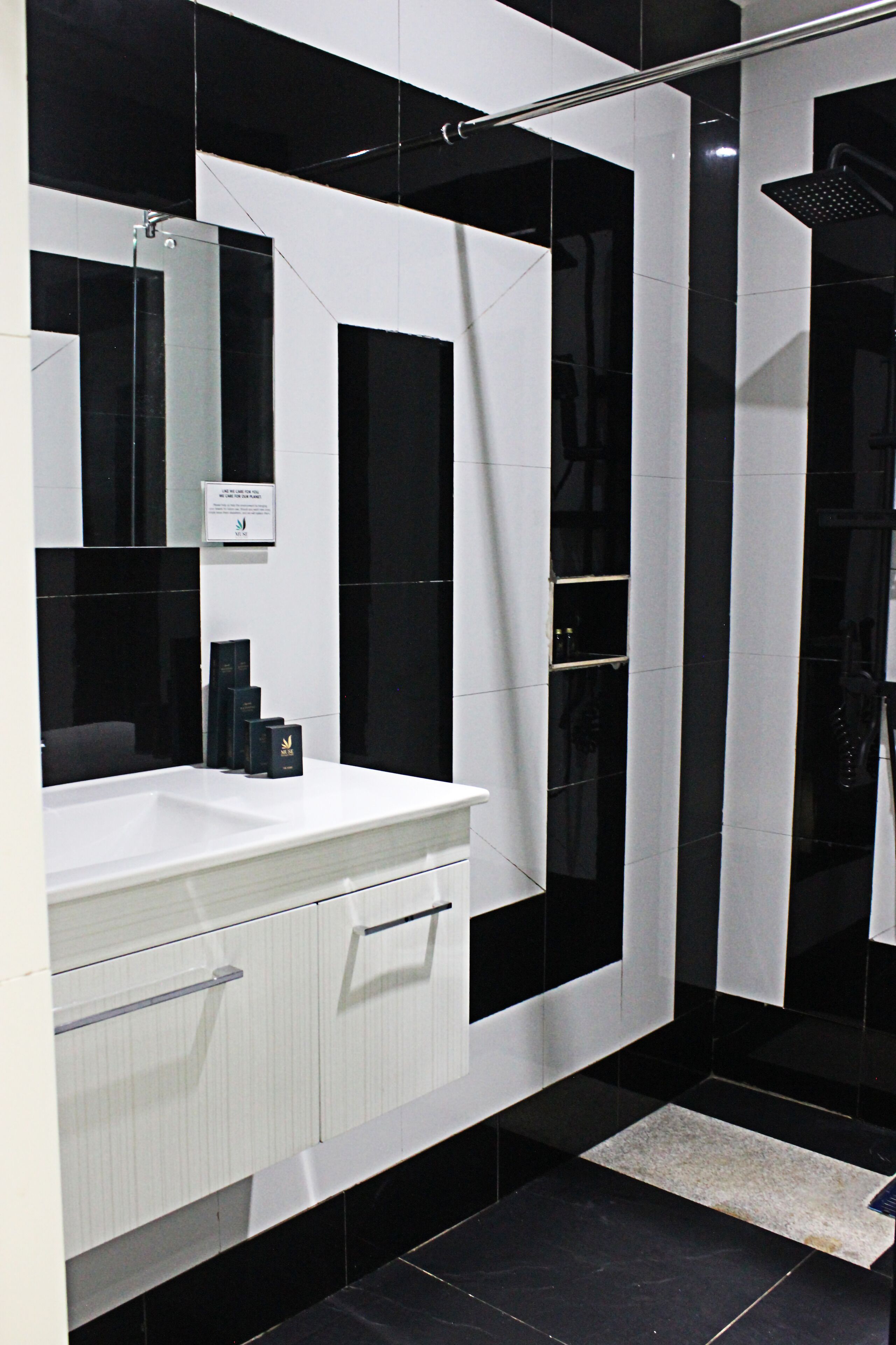 Un baño moderno con un espejo grande, un lavamanos blanco y una zona de ducha con azulejos negros.