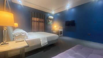 A hotel room with a bed, a desk with a lamp, a chair, a small table, and a TV mounted on the wall.