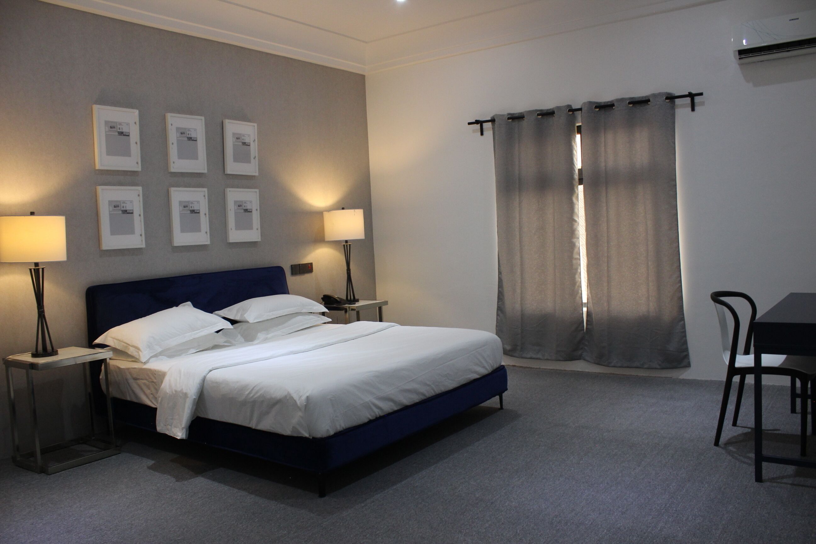 A neatly made bed with white linens, two bedside lamps, a small table, and a chair.