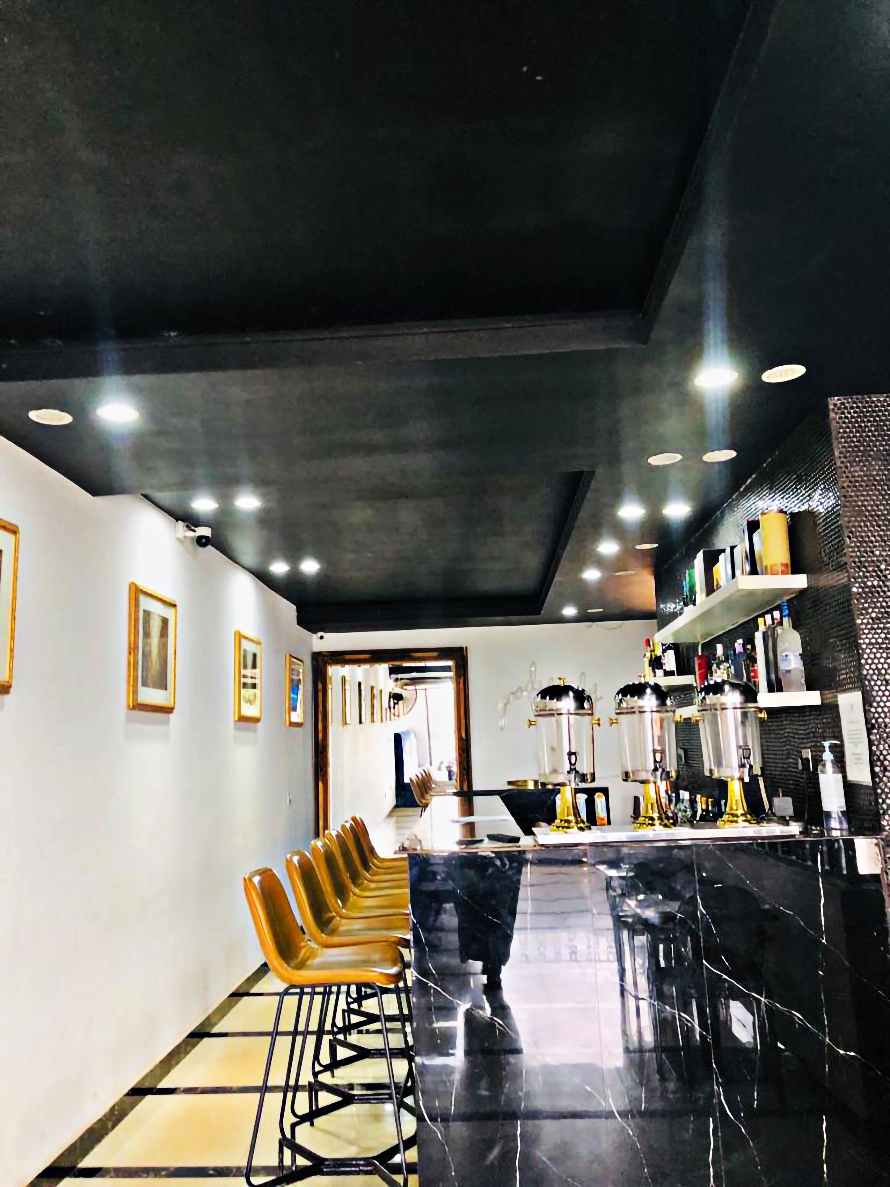 A modern bar area with a black countertop, bar stools, and a mirrored wall.