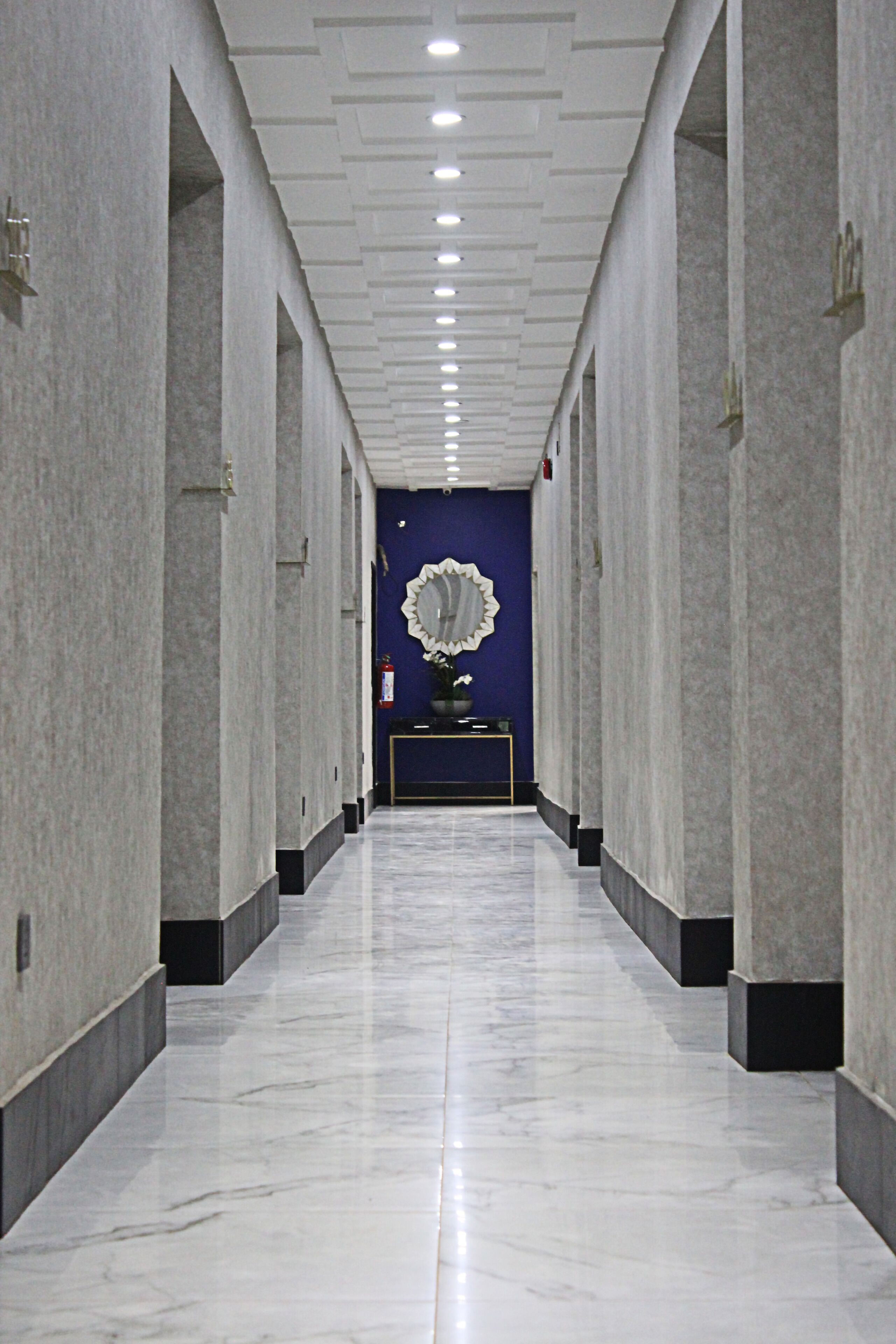 A hallway with marble floors and white walls, leading to a reception area with a blue wall and a decorative mirror.