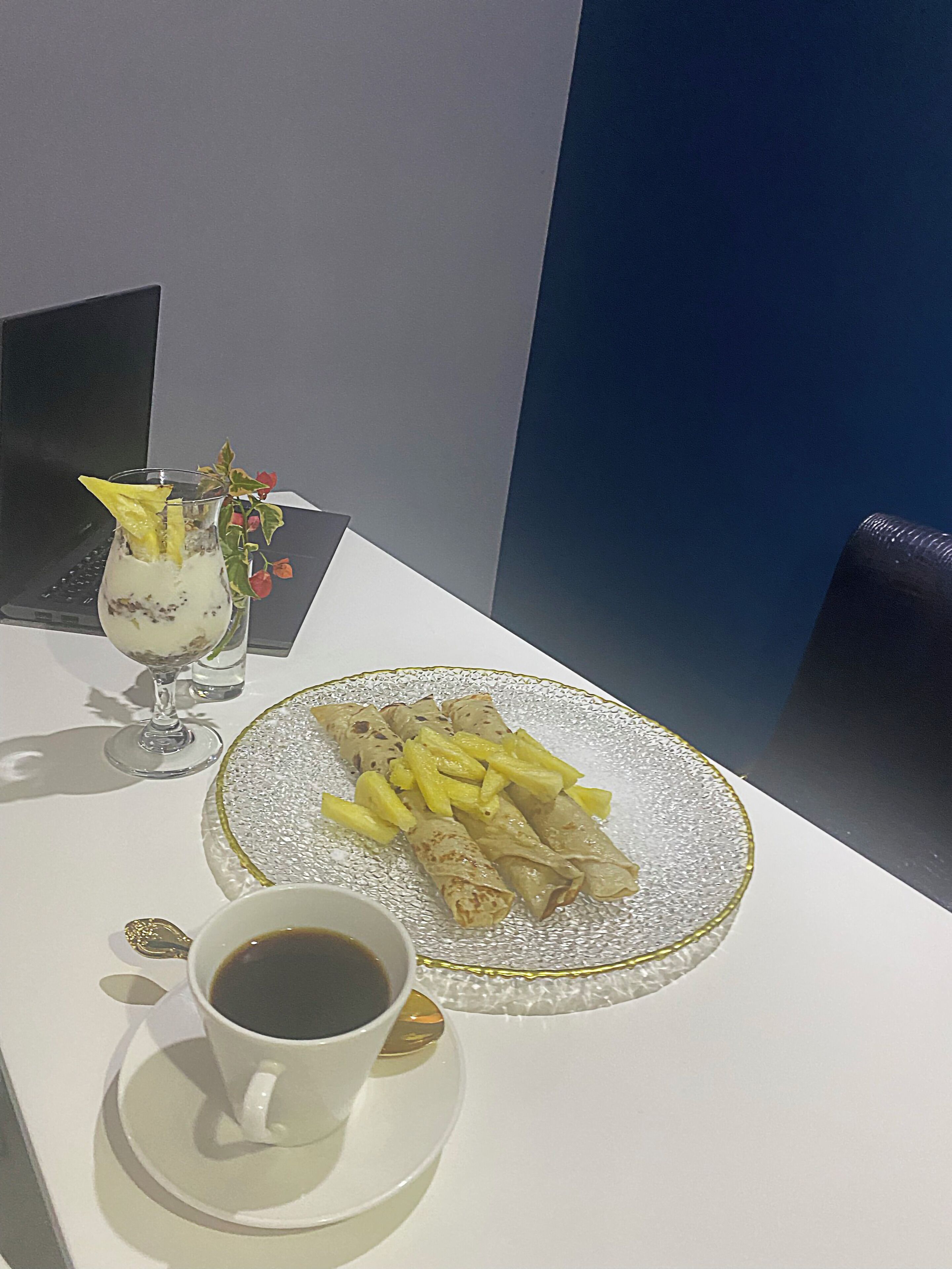 A table with a plate of crepes, a cup of coffee, and a glass of dessert.