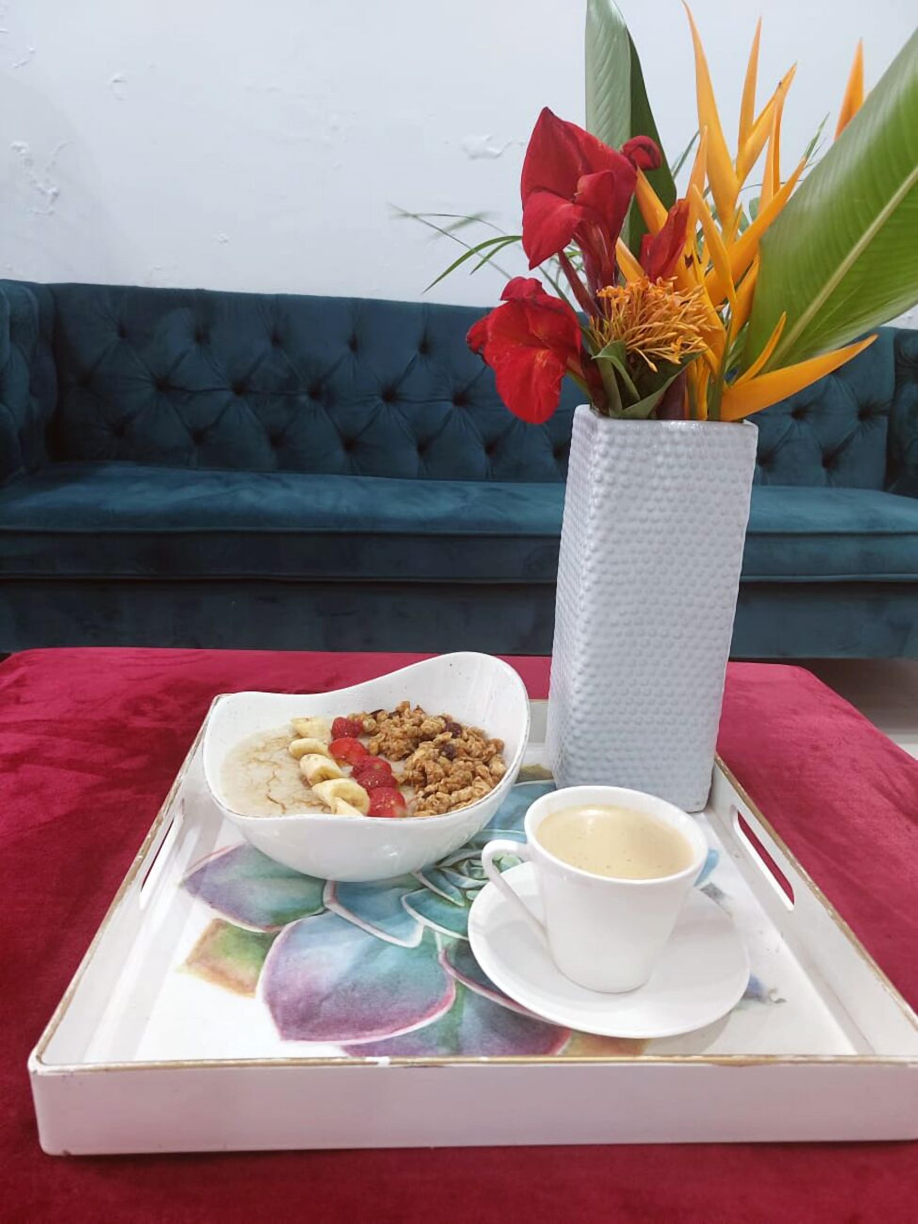 Una bandeja con un tazón de cereal, una taza de café y un florero sobre una mesa con un mantel rojo.