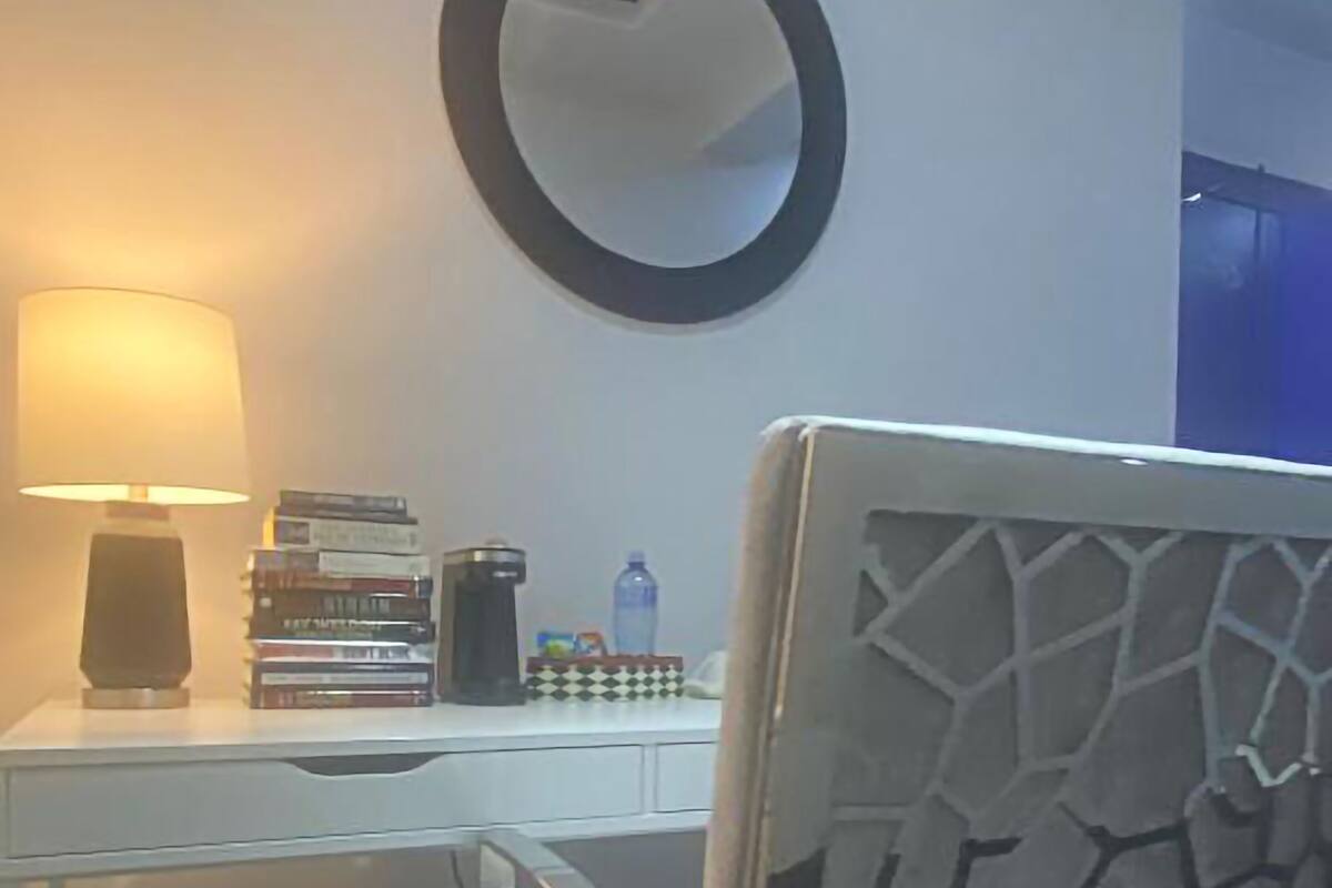 Ein Hotelzimmer mit Schreibtisch, einem Stuhl mit geometrischem Muster, einem runden Spiegel und einer Lampe.