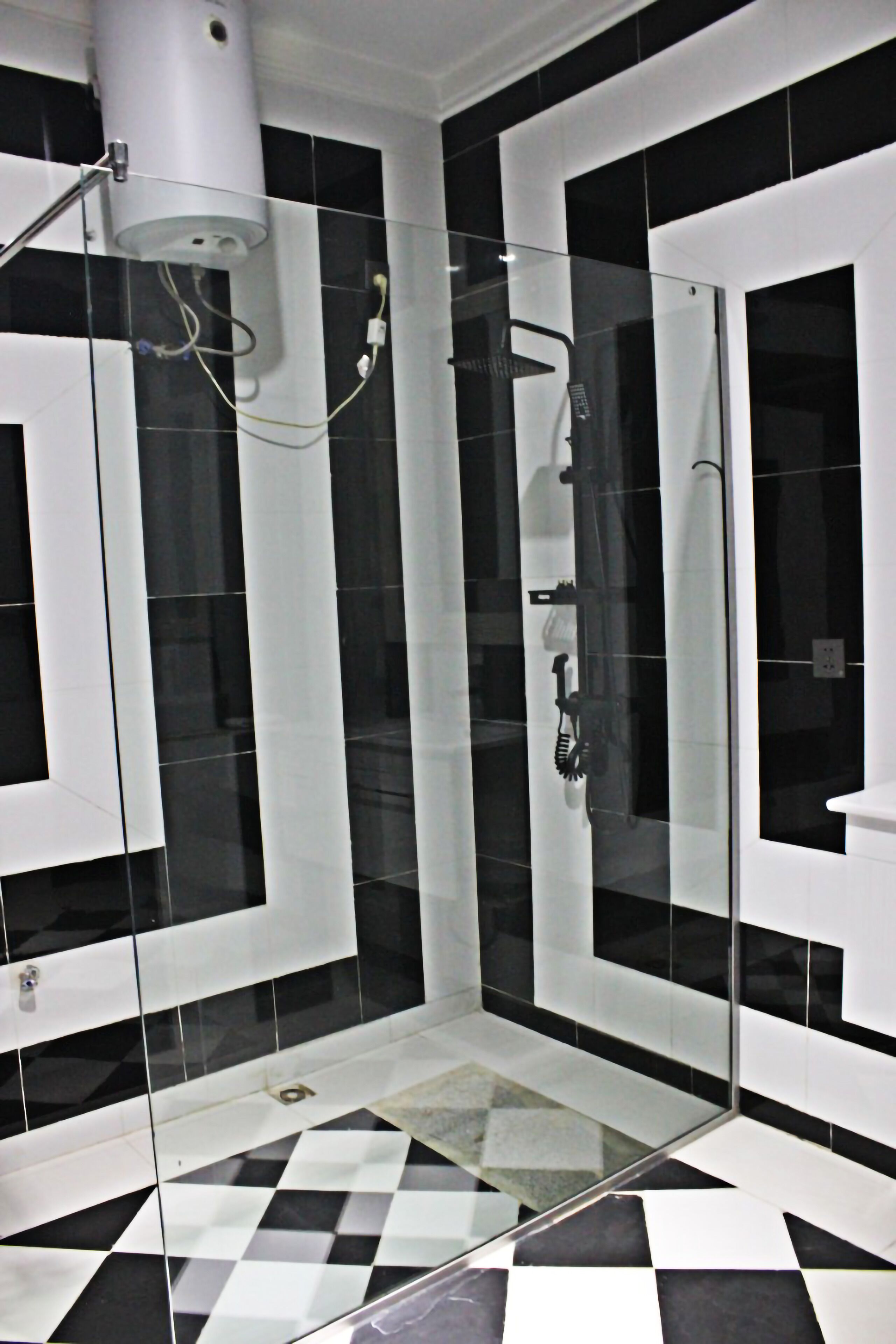 Un baño moderno con baldosas blancas y negras a cuadros, cabina de ducha de vidrio y lavamanos blanco.