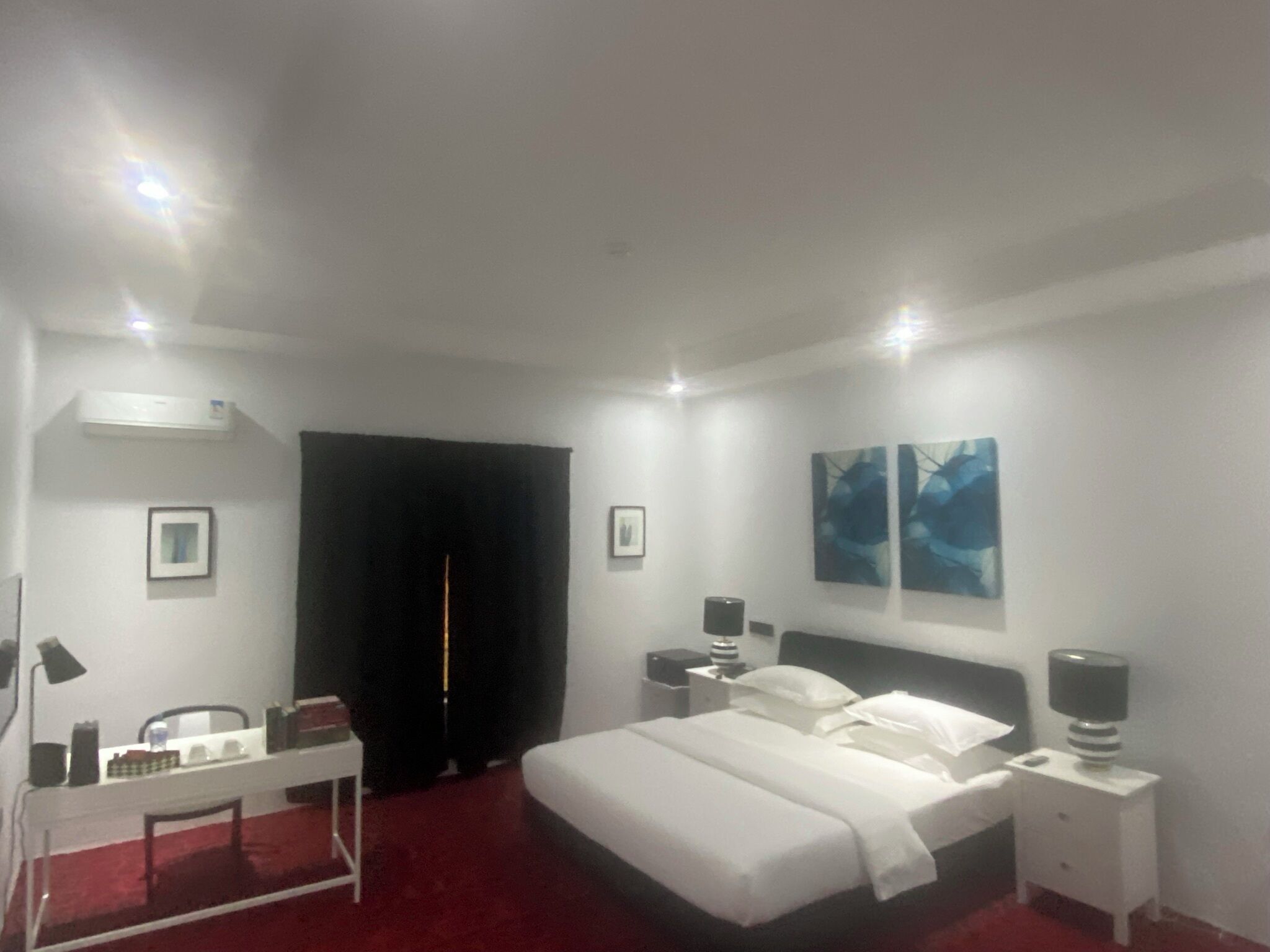A hotel room with a bed, bedside tables, a desk, and artwork on the walls.