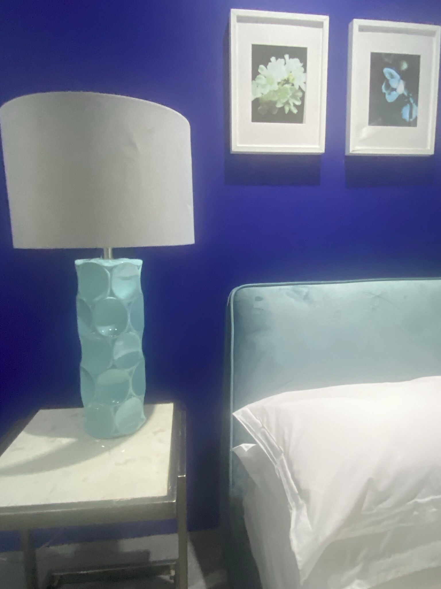 A room with a bed, a nightstand with a lamp, and two framed pictures on the wall.