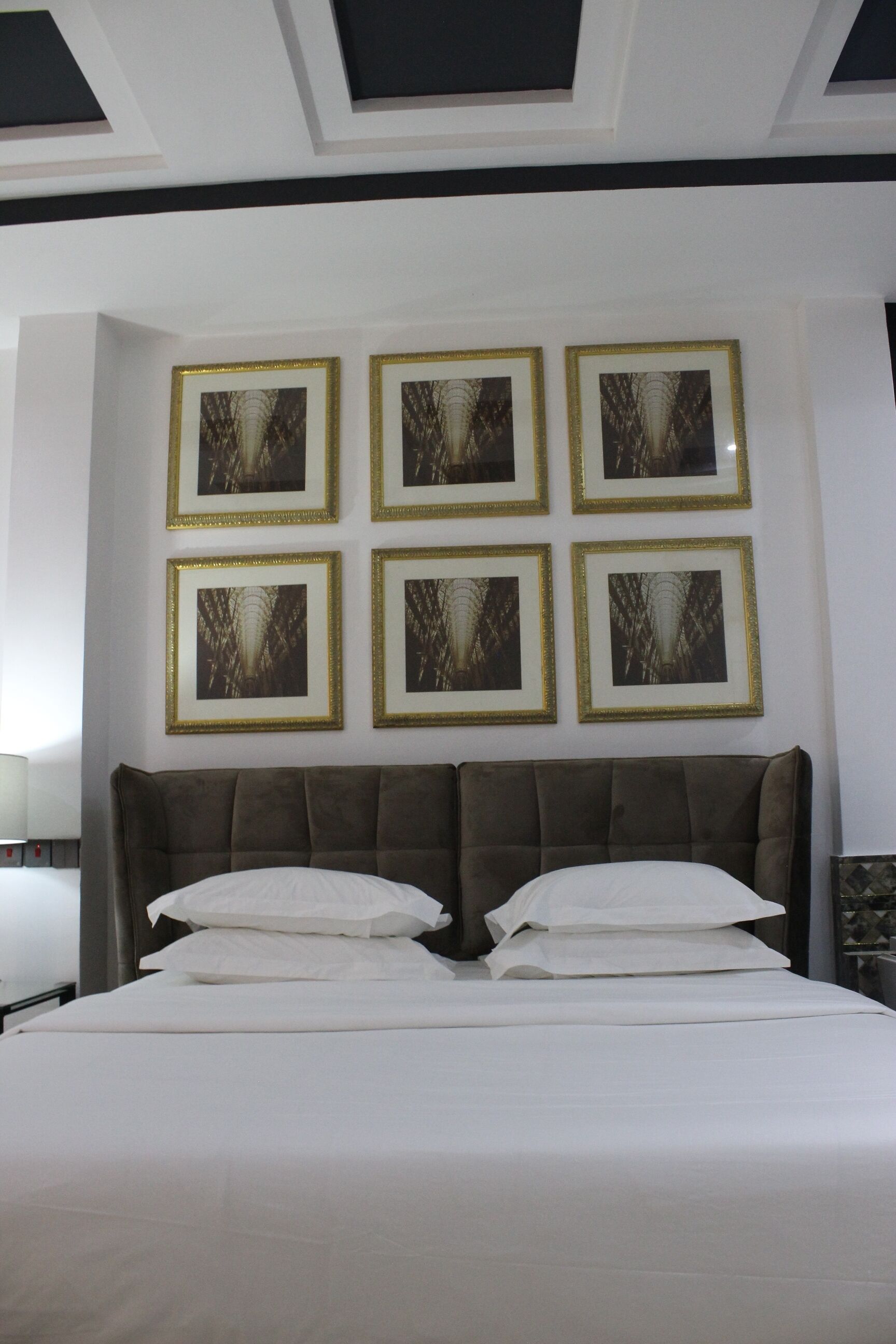 Une chambre d’hôtel avec un grand lit, une tête de lit et six tableaux encadrés accrochés au mur.