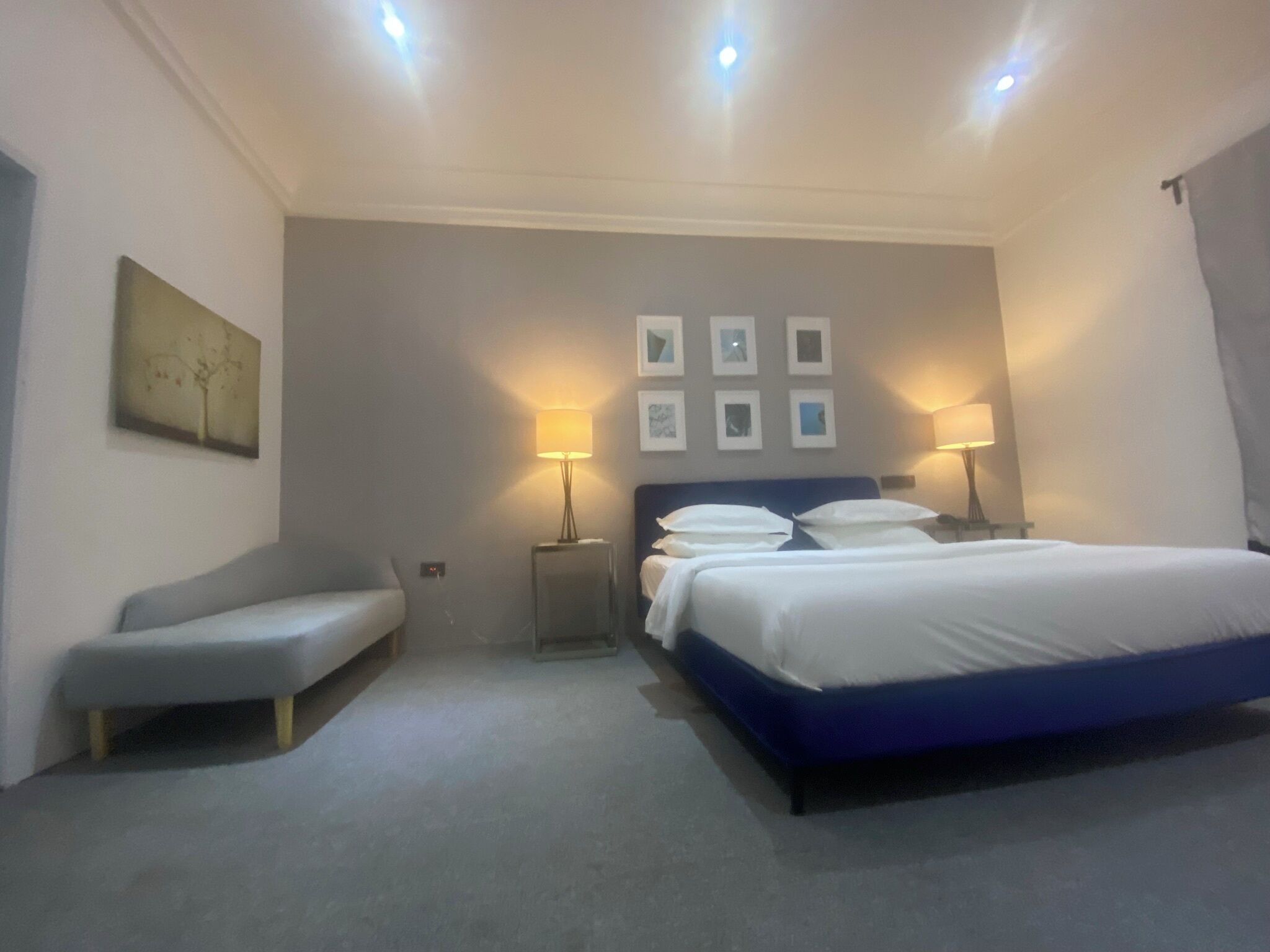 A hotel room with a large bed, two bedside tables with lamps, a bench, and a wall with framed pictures.