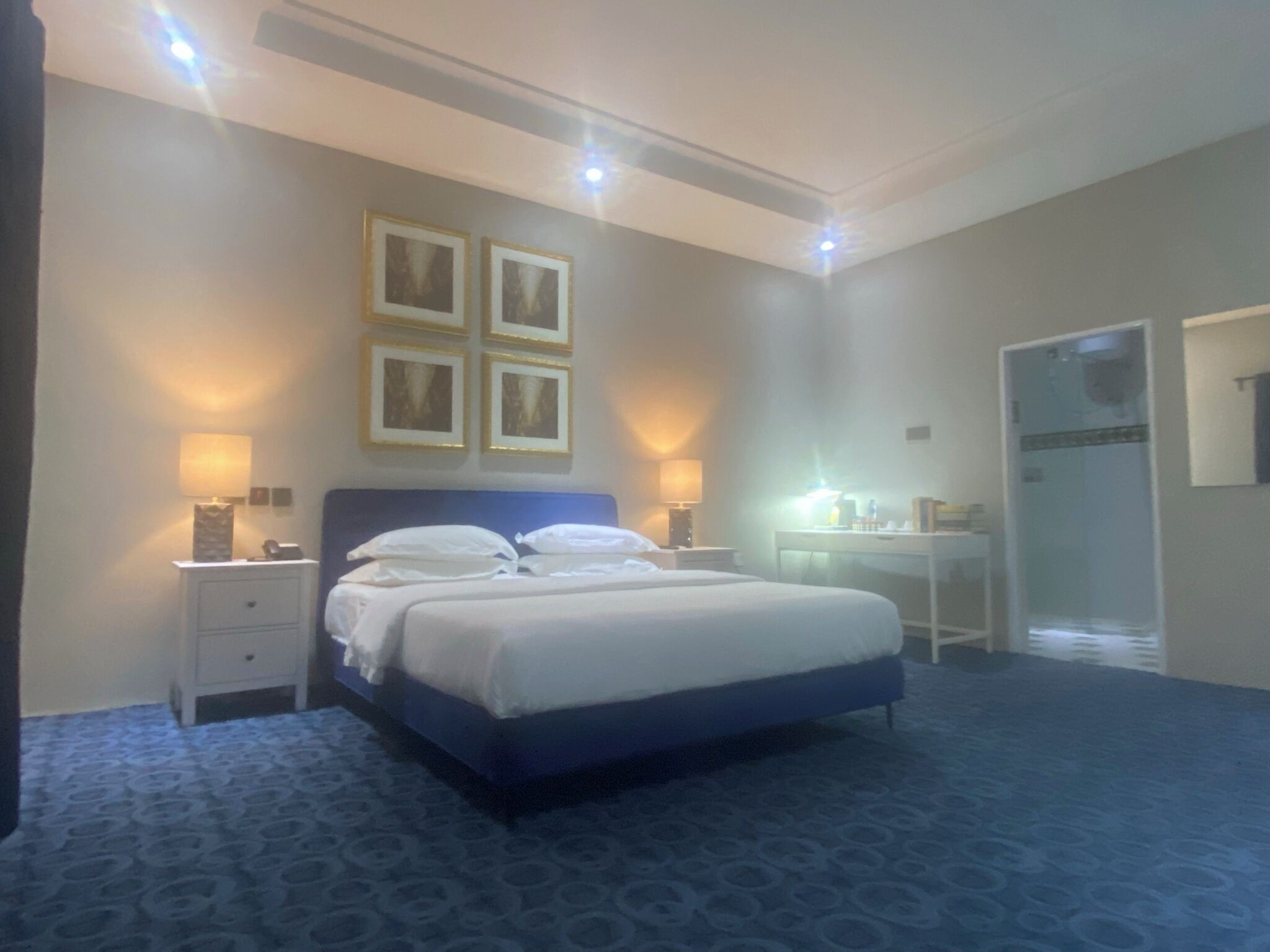 A hotel room with a large bed, two bedside tables with lamps, a desk, and a mirror.