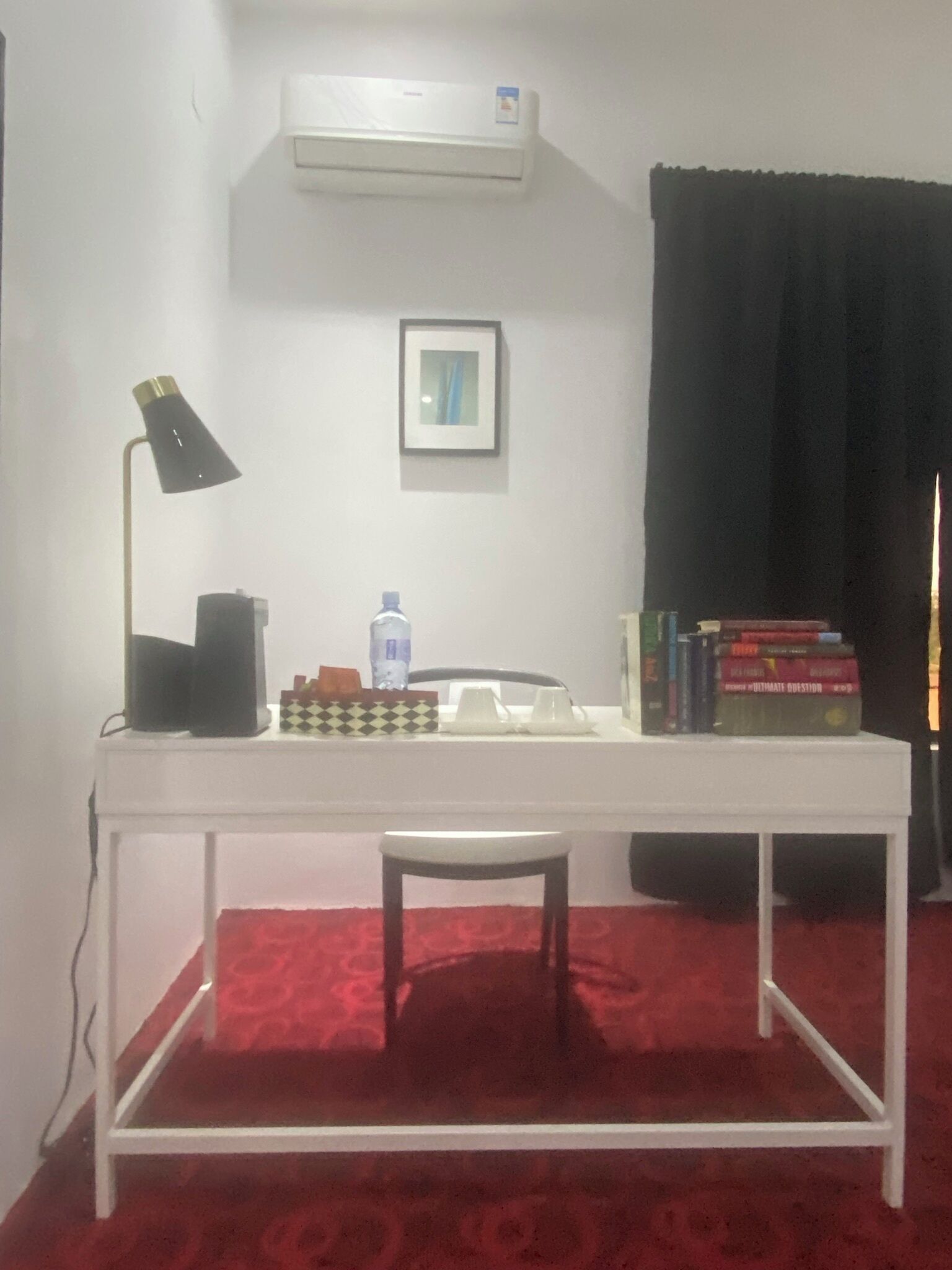 A room with a white desk, a black desk lamp, a framed picture, a water bottle, and a stack of books.