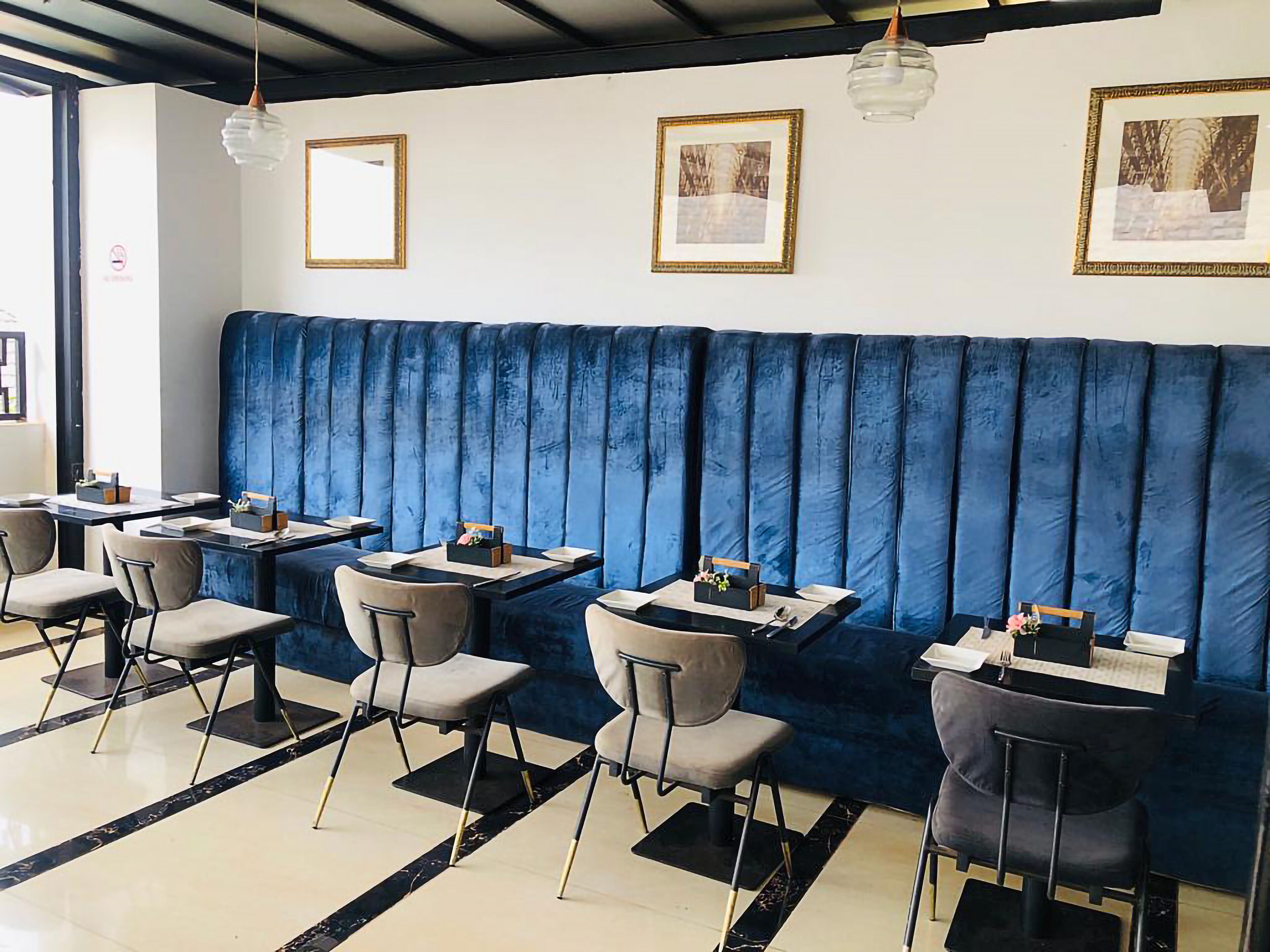 A restaurant with a blue cushioned booth seating area, tables with chairs, and framed pictures on the walls.