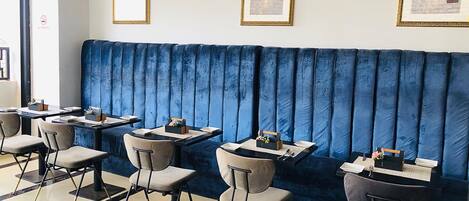 A restaurant with a blue cushioned booth seating area, tables with chairs, and framed pictures on the walls.