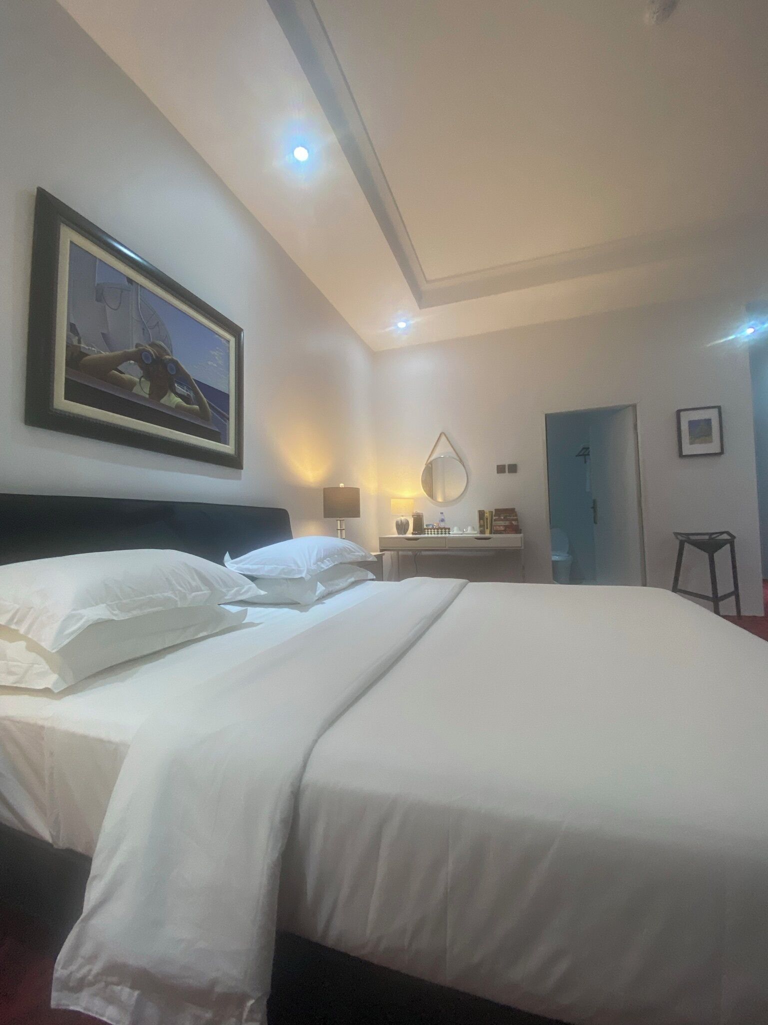 A hotel room with a large bed, a bedside table, a mirror, and a framed picture on the wall.