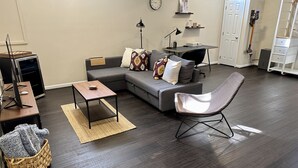 A modern living room with a gray sectional sofa, a wooden coffee table, a woven basket, and a dark wood floor.