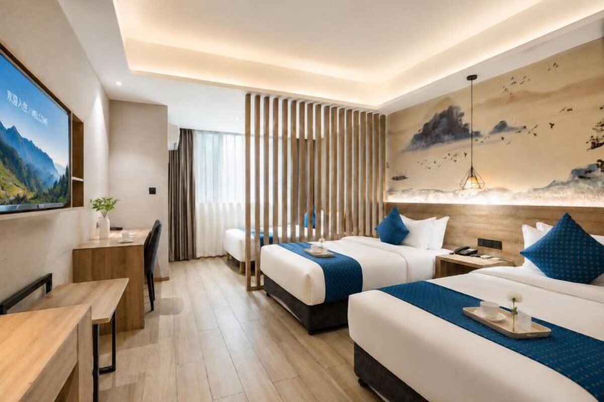A hotel room with two beds, a desk, a TV, and a painting on the wall.