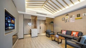 Een moderne woonkamer met een houten vloer, een bank, een salontafel en een aan de muur bevestigde televisie.