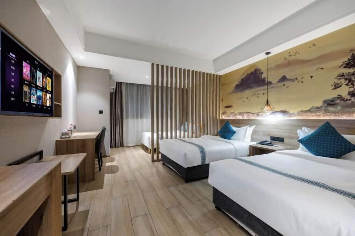 Une chambre d’hôtel avec deux lits, un bureau et un écran de télévision diffusant différentes chaînes.