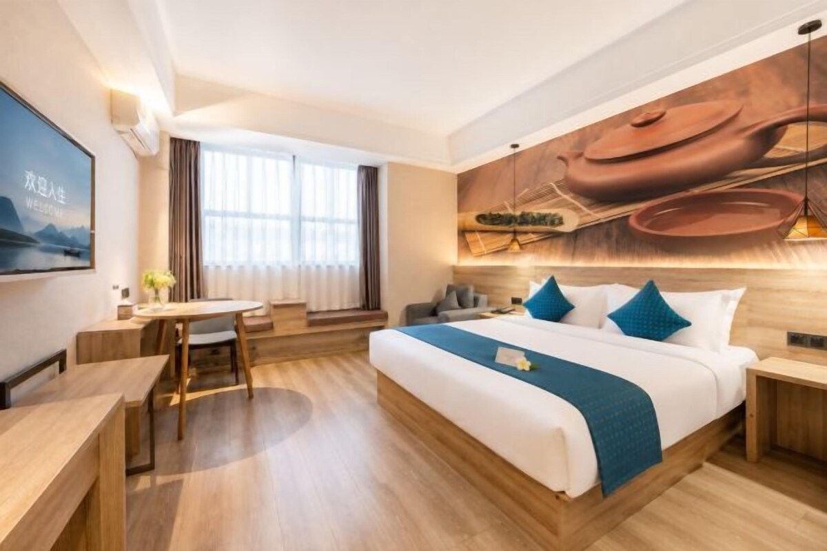 A hotel room with a bed, bedside tables, a desk, and a large window.