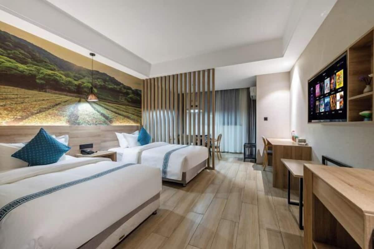 Une chambre d’hôtel moderne équipée de deux lits, d’un bureau et d’un grand écran numérique diffusant du contenu.