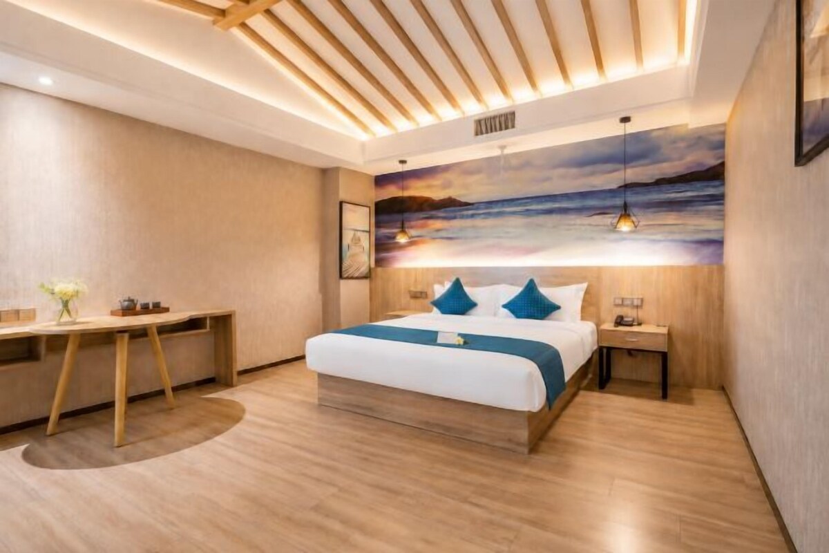 A modern hotel room with a large bed, a desk, and a view of the sea.