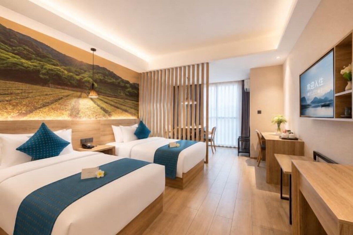 A hotel room with two beds, a desk, a chair, a TV, and a large window.