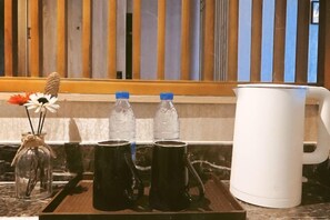 Un plateau contenant deux tasses noires, deux bouteilles d’eau, une cafetière blanche et un bocal en verre avec des fleurs, le tout posé sur un comptoir en marbre.