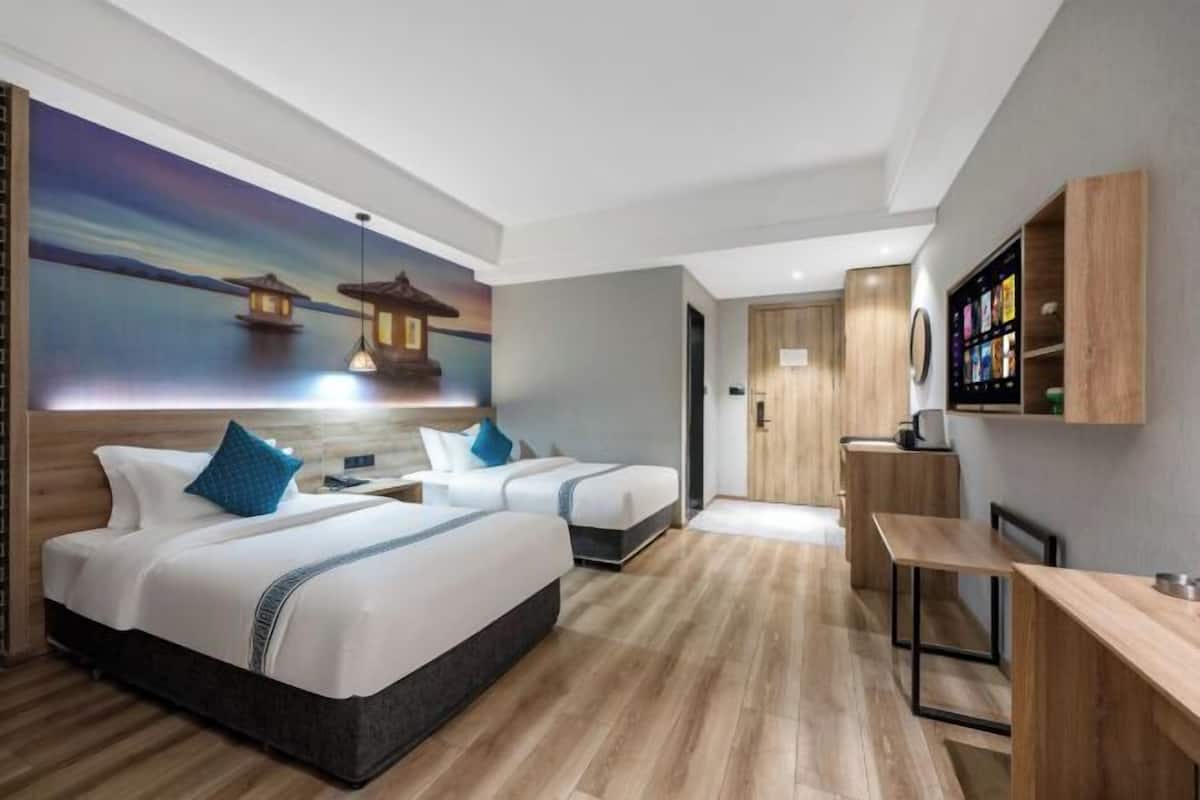 Une chambre d’hôtel avec deux lits, un bureau, une télévision et une fresque murale représentant un coucher de soleil sur l’eau.