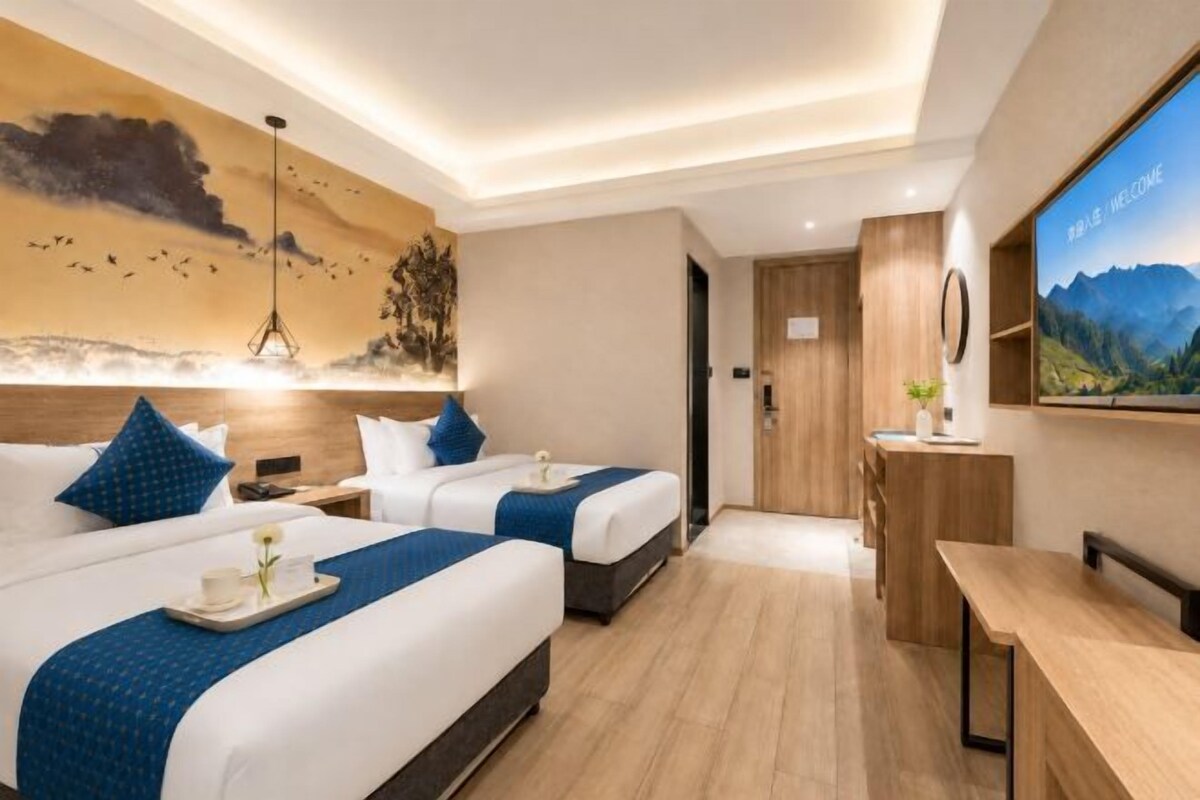 A hotel room with two beds, a desk, a TV, and a painting on the wall.