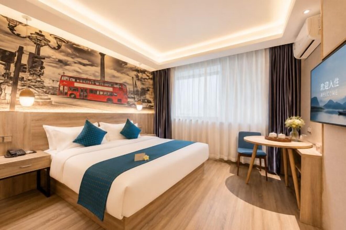 A hotel room with a bed, bedside table, and a small round table with a vase.