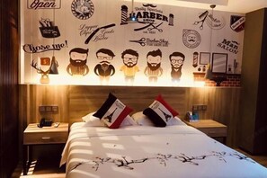 Une chambre d’hôtel comprenant un lit, des tables de chevet et un mur décoré d’œuvres d’art sur le thème d’un salon de coiffure.