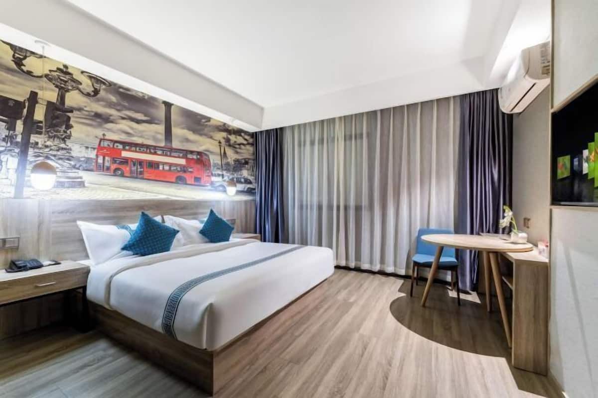 Une chambre d’hôtel comprenant un lit, un bureau, une chaise, une fenêtre avec des rideaux et une fresque murale.