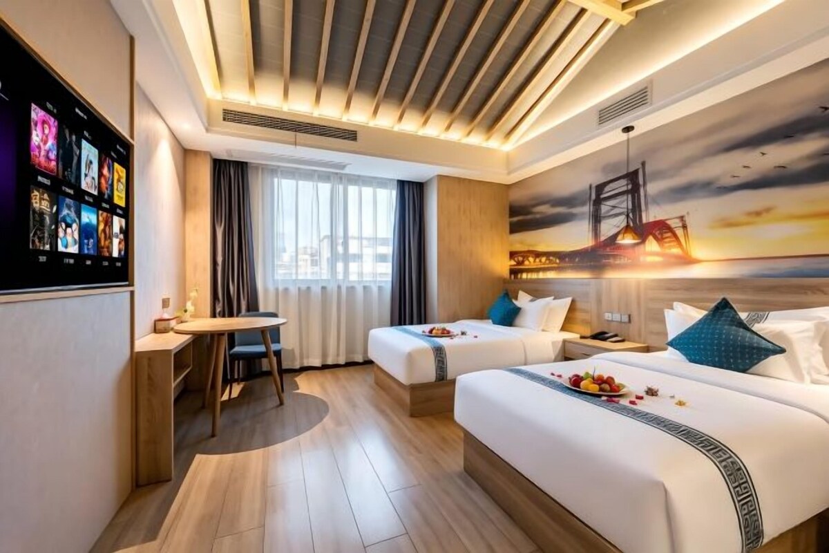 A hotel room with two beds, a desk, and a large window.