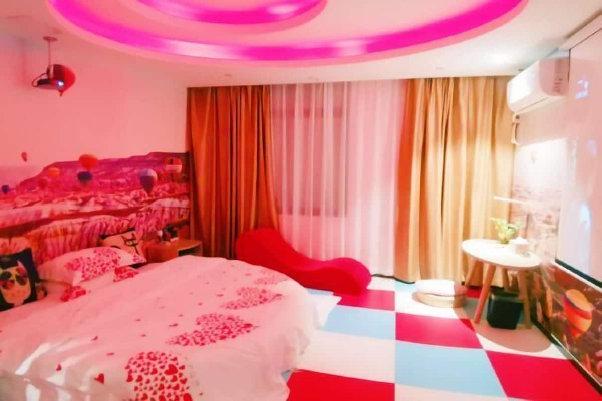 Une pièce avec un lit, des rideaux, une petite table et une chaise rouge.