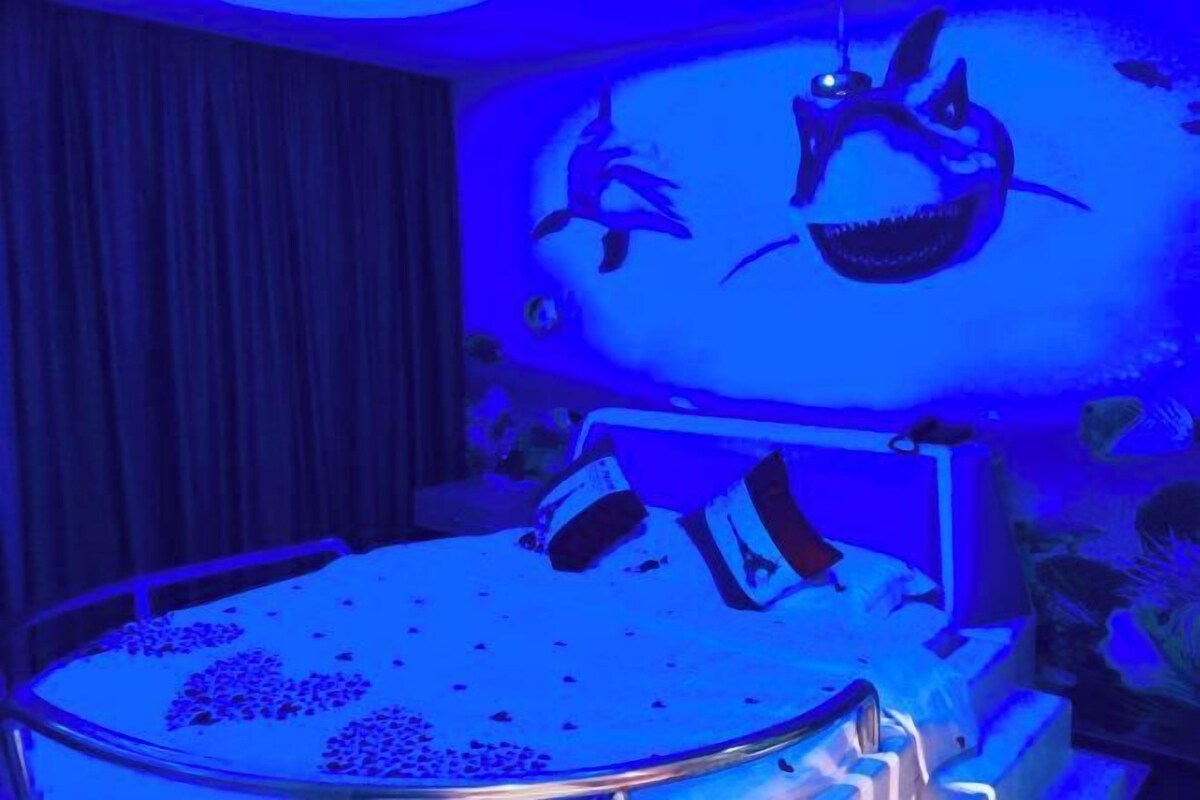 Une chambre avec un lit, un grand écran sur lequel est projetée une image de requin, et un rideau.