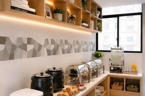 A breakfast bar with coffee makers, a juice dispenser, and a variety of pastries.