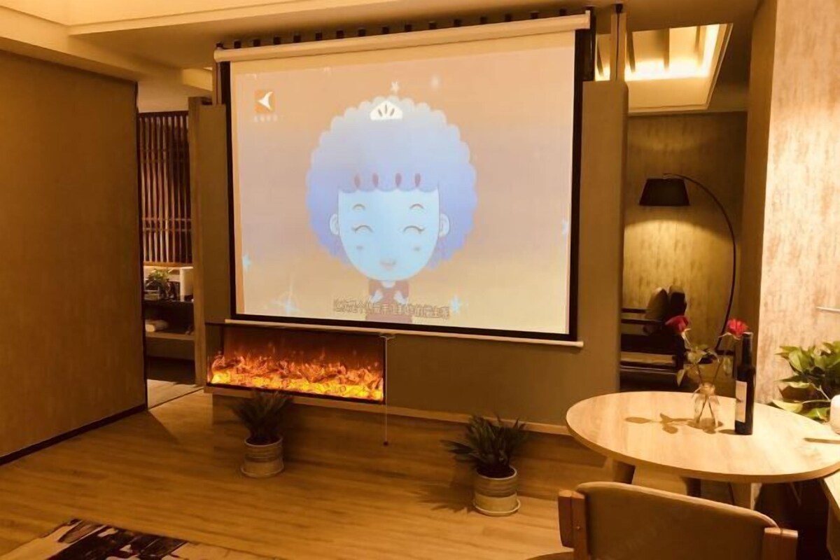 Une pièce chaleureuse avec une cheminée, un écran de projection sur lequel est diffusé un personnage de dessin animé, et une petite table sur laquelle est posé un vase.