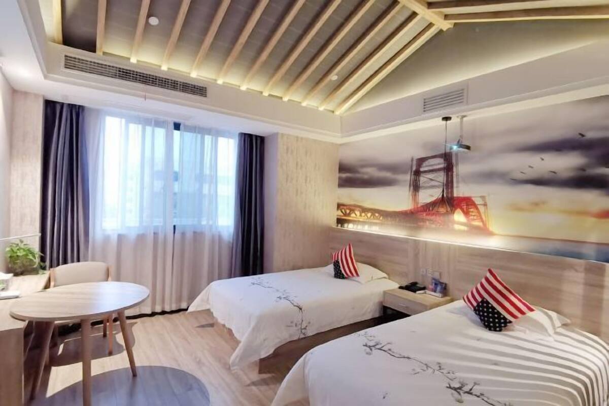 Une chambre d’hôtel avec deux lits, une table ronde et une grande fenêtre avec des rideaux.