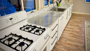 A kitchen with a white stove, a sink, and a window with curtains. - Spacious, private and peaceful 1st floor Apartment on Fly Creek  (Fly Creek)