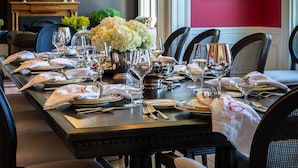Una mesa de comedor dispuesta con varios platos, vasos y cubiertos, rodeada de sillas tapizadas.