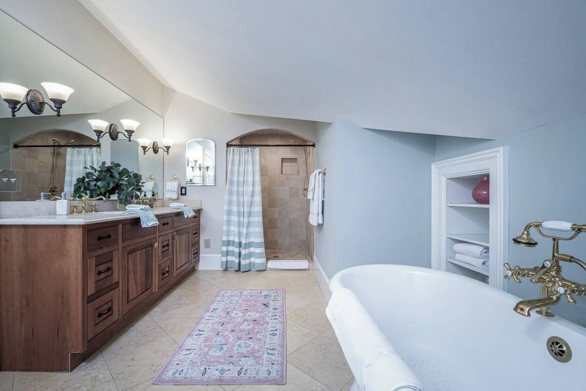 A bathroom with a bathtub, a wooden vanity, a large mirror, and a shower area.
