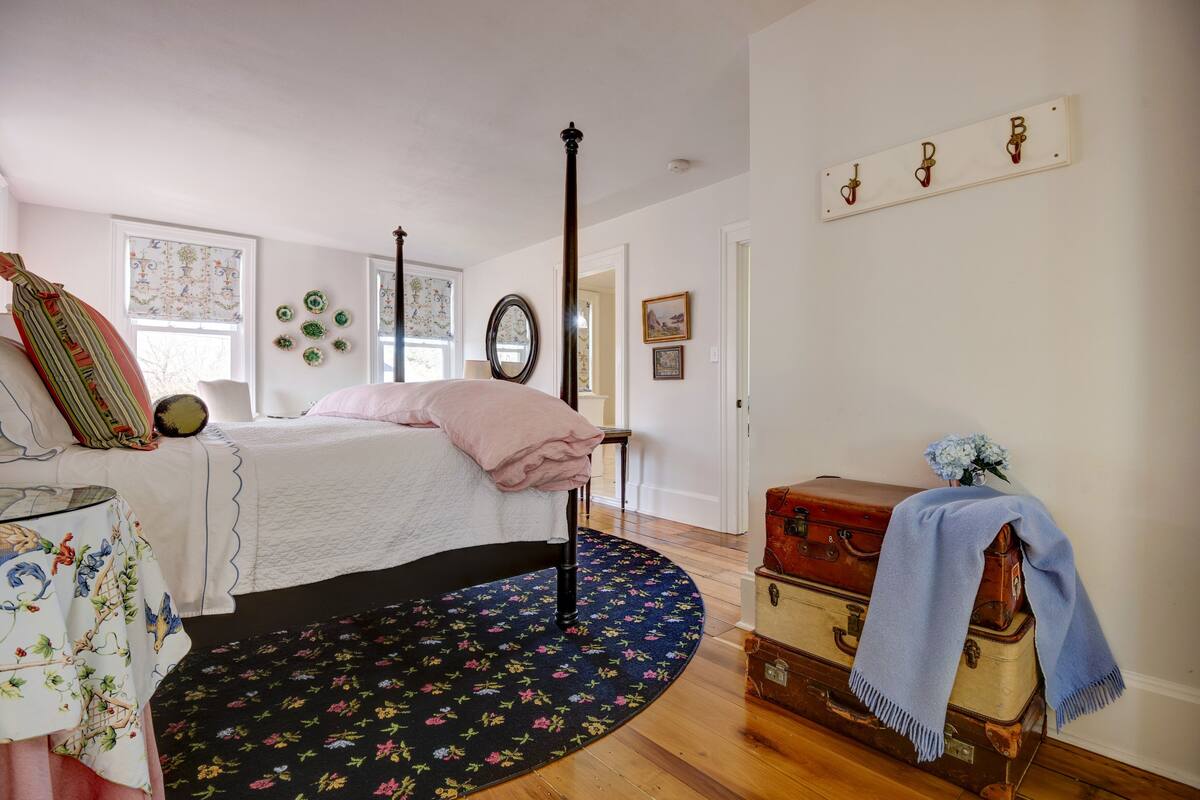A bedroom with a four-poster bed, a round rug, and vintage suitcases.